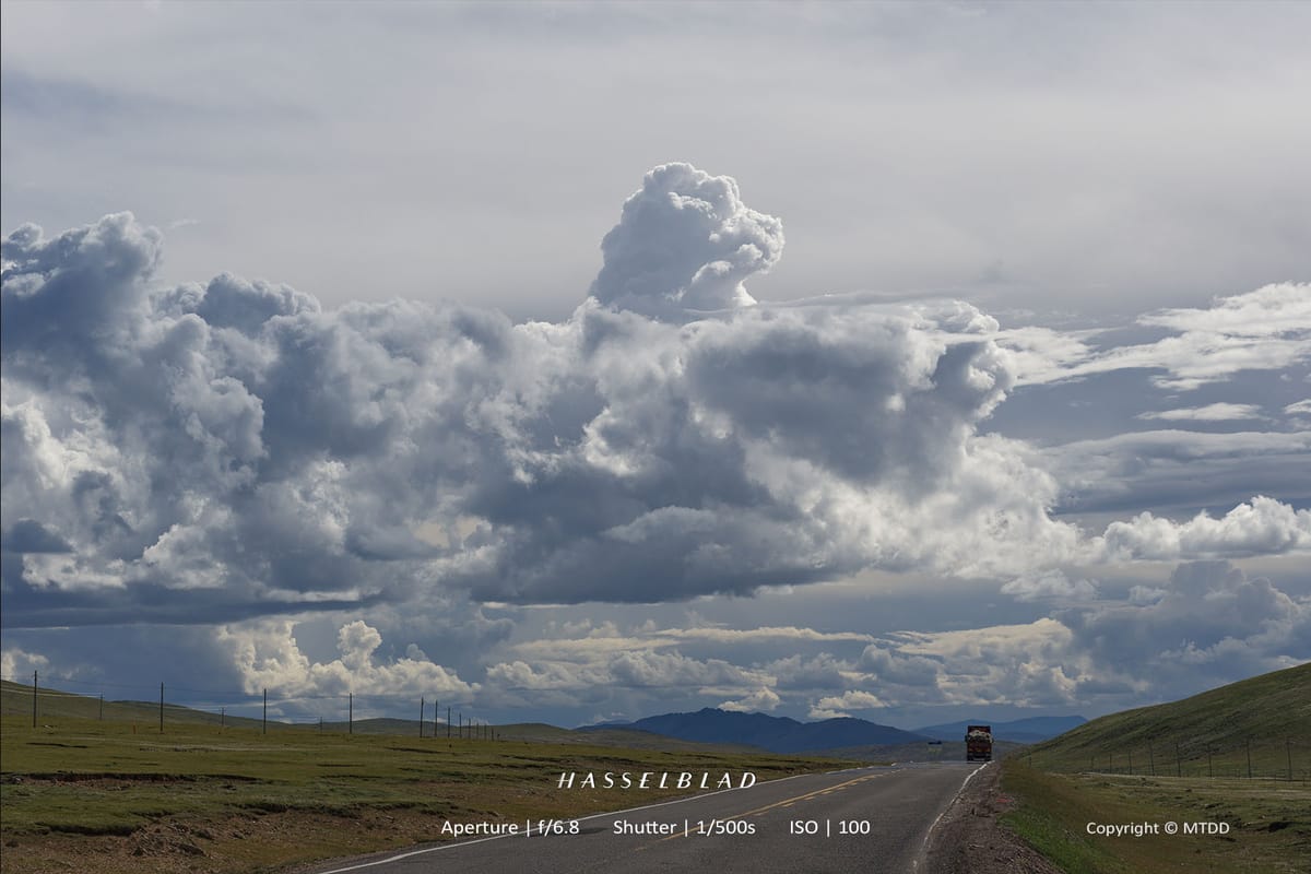 Dramatic cloudy sky over empty highway through grassy plains with distant mountains