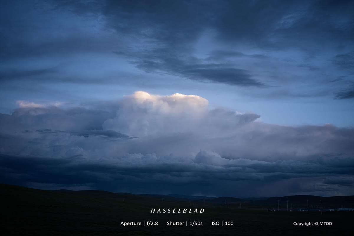Dark stormy clouds billow over shadowy landscape with bright illuminated cloud center