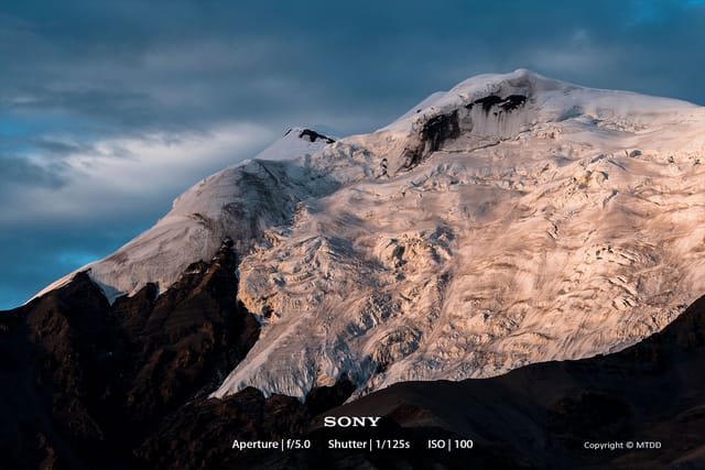 Majestic Nyenchen Tanglha Mountain silhouetted against a vibrant sunset sky, casting long shadows over Tibetan plateau