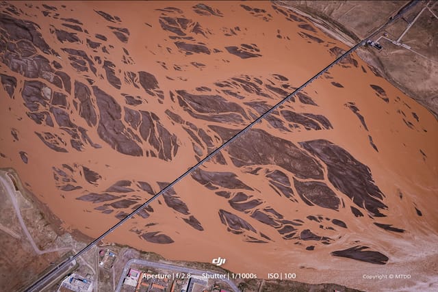 Green diesel locomotive NJ20008 crossing elevated railway bridge above dramatic Tuotuo River landscape with mountains in background