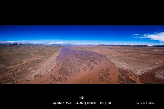 Panoramic aerial view of winding muddy river cutting through arid desert landscape under vivid blue sky with scattered clouds