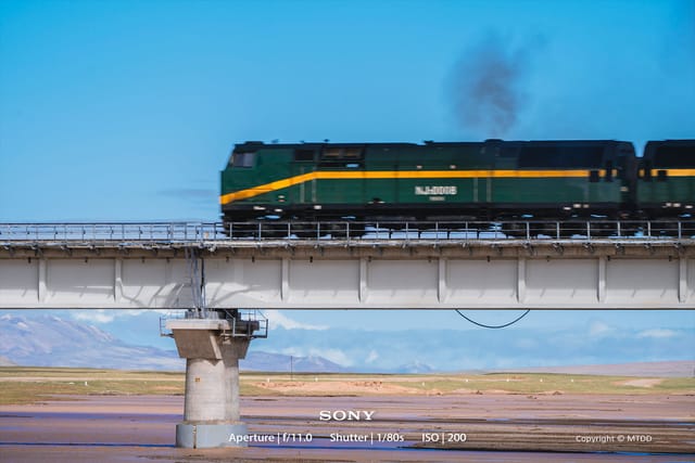 NJ20008 diesel locomotive traversing the expansive Qinghai-Tibet Plateau with dramatic mountain landscape in background