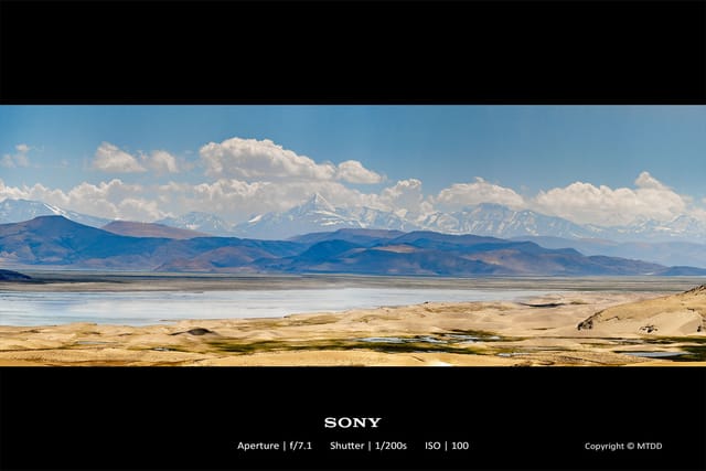 Snow-capped mountain range overlooking barren salt flat landscape with scattered water pools
