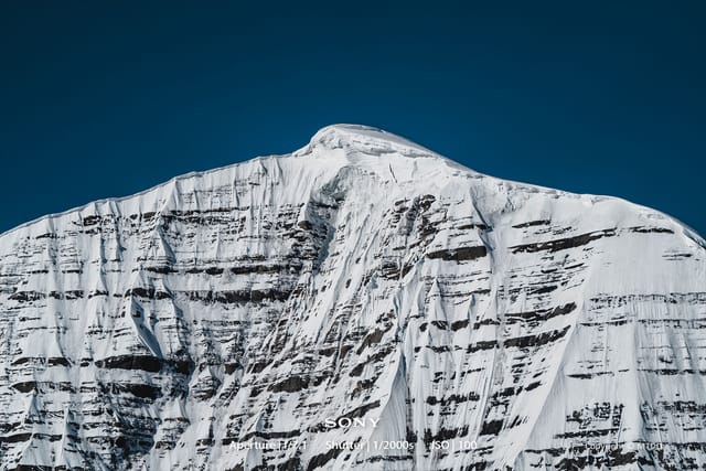 Snow-covered mountain peak with steep rocky cliffs and glacial formations against deep blue sky