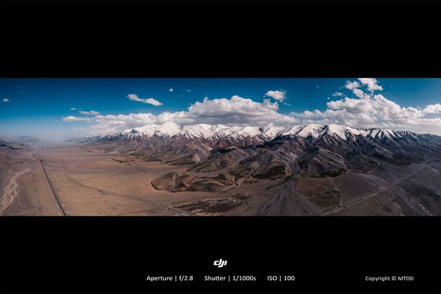 Snowy mountain peaks rising above arid desert valley with long highway stretching into distance