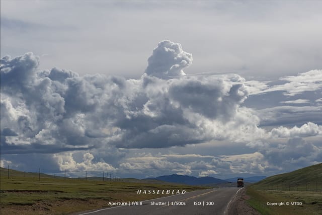 Dramatic cloudy sky over empty highway through grassy plains with distant mountains