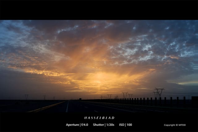 Dramatic sunset illuminates stormy clouds over empty highway with power transmission towers silhouetted against golden sky